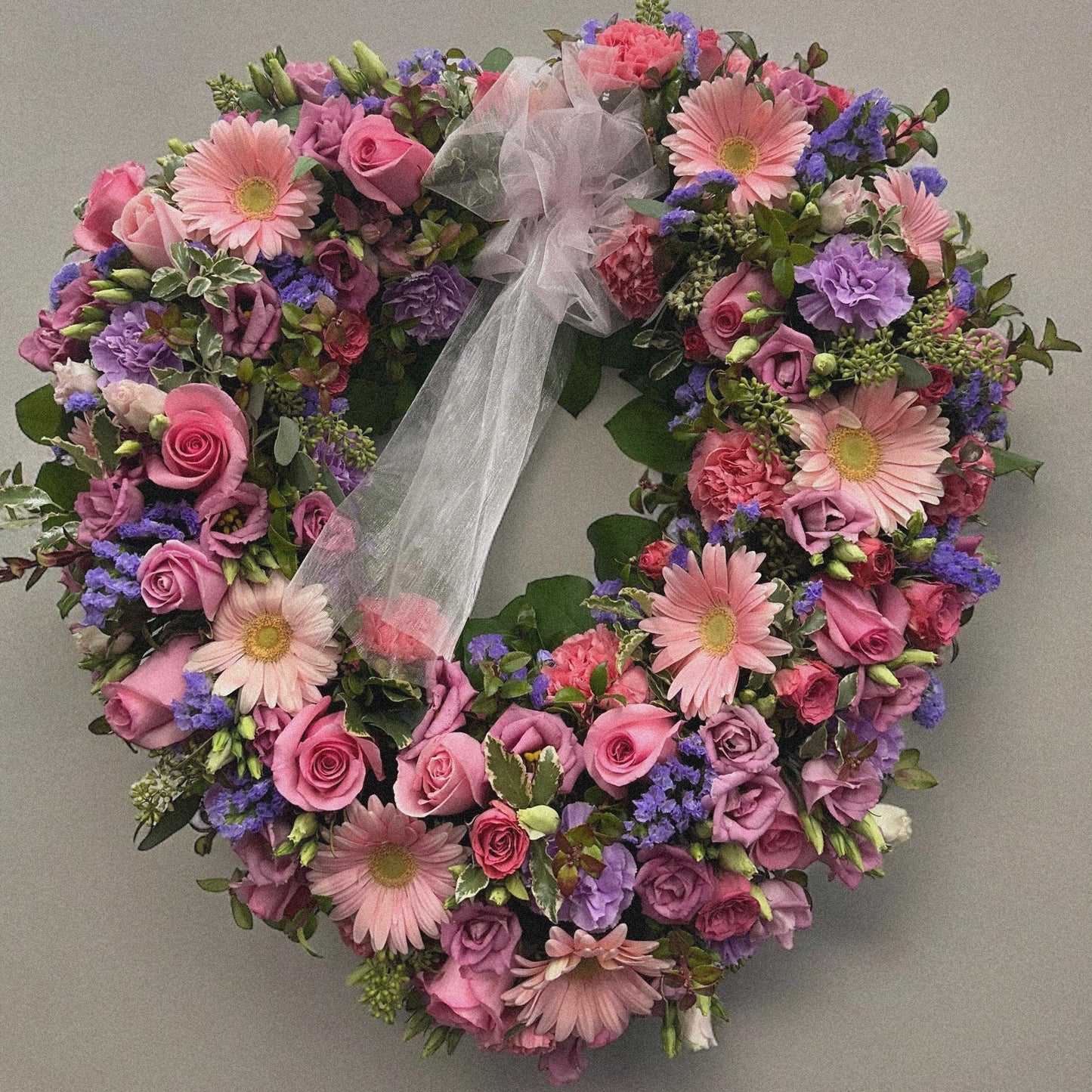 Heart-shaped spring wreath with pink roses and purple blooms, a funeral tribute for love and remembrance. Best in Toronto.