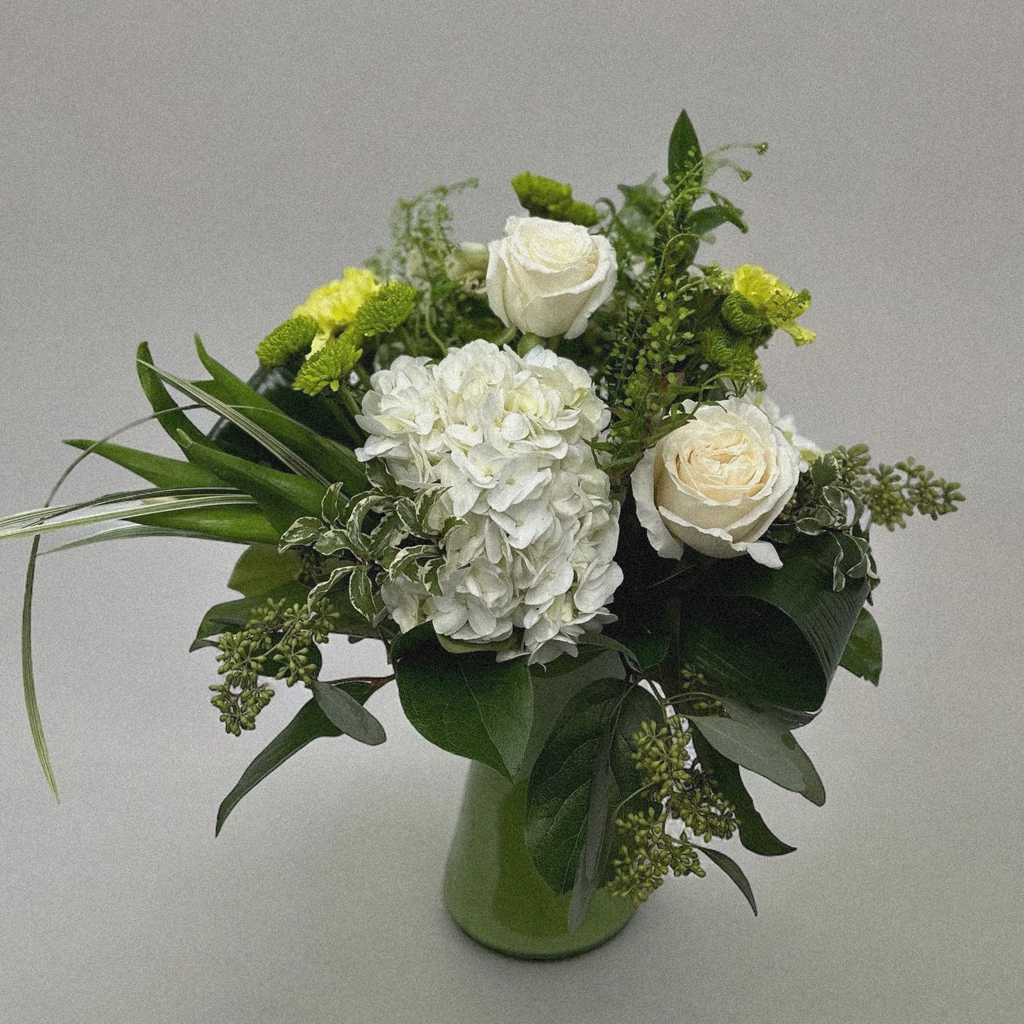 Vintage Charm bouquet with white roses, hydrangeas, green poms, greenery in green vase. Chic florist arrangement, best in Toronto & GTA.