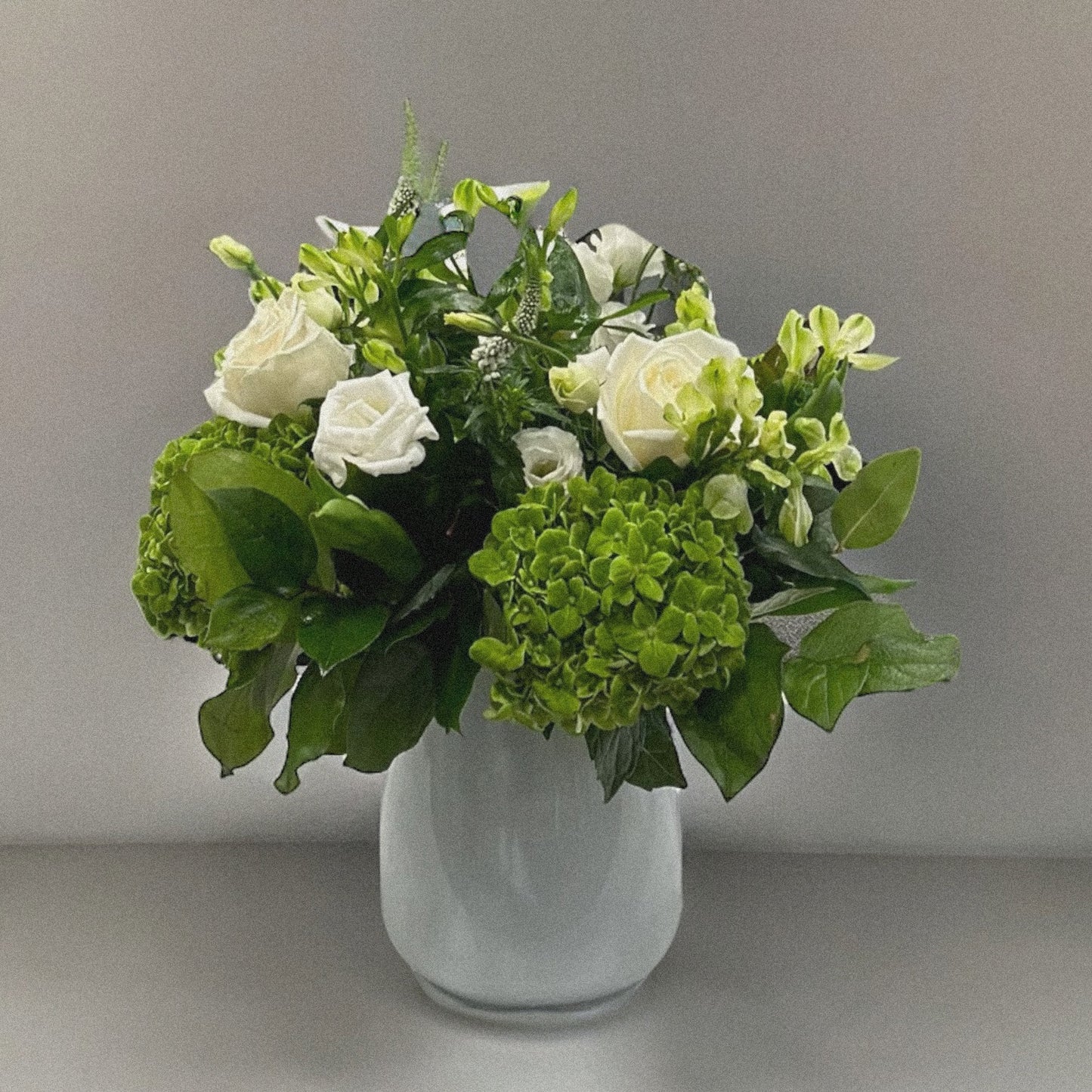 Luxury flower arrangement with white roses and green foliage in a white vase, available for same day delivery in Toronto and GTA.