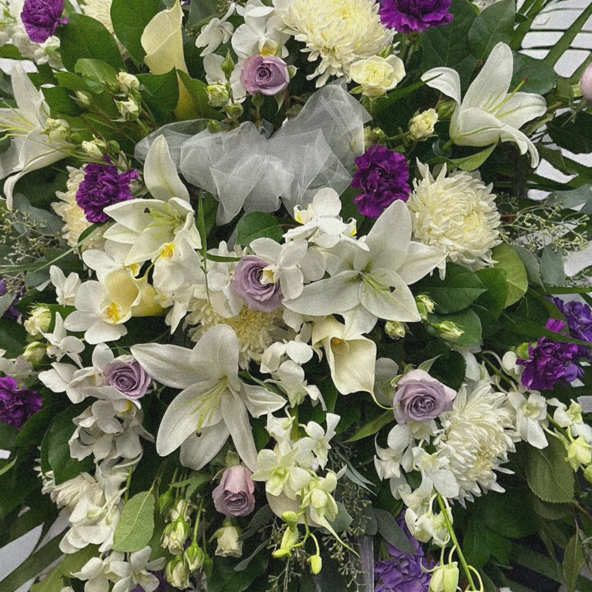 Regency Splendor floral spray with white lilies, purple blooms; a sympathy funeral arrangement available for same-day delivery in Toronto.