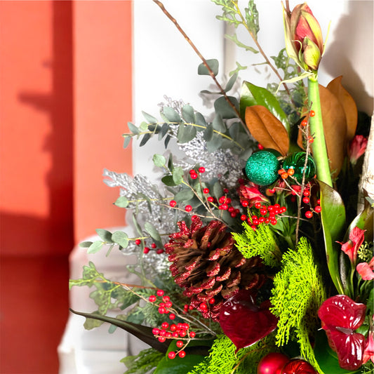 Festive holiday vase arrangement featuring evergreens, ornaments, red flowers, and seasonal textures by Roza Flowers.