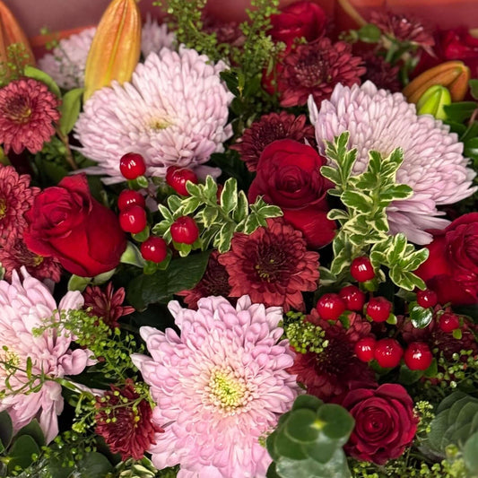 Bouquet of flowers with red and pink colors in a decorative paper wrap against a neutral background.