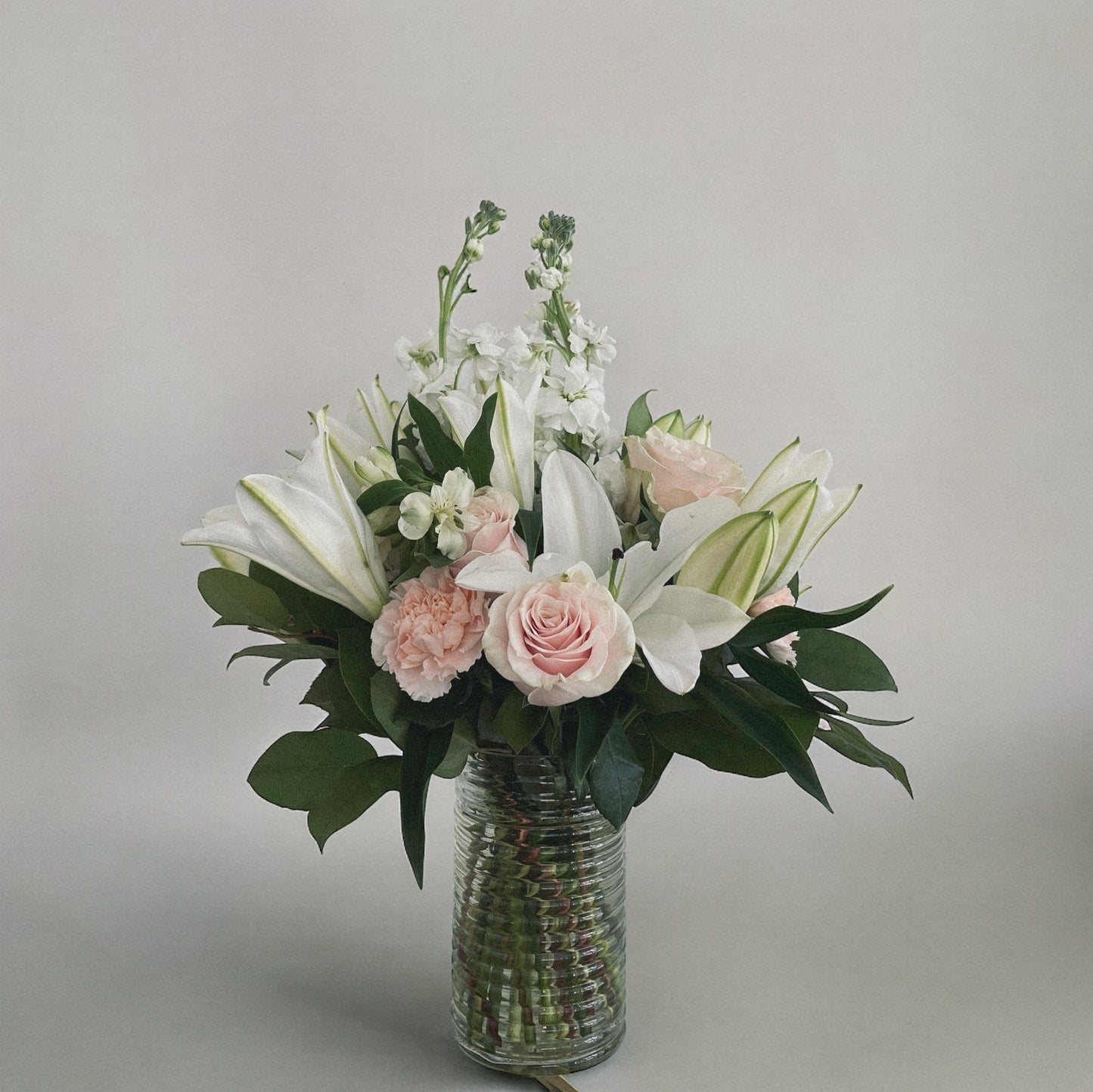 Elegant sympathy flower arrangement with white roses, lilies, and greenery, designed to express love and remembrance