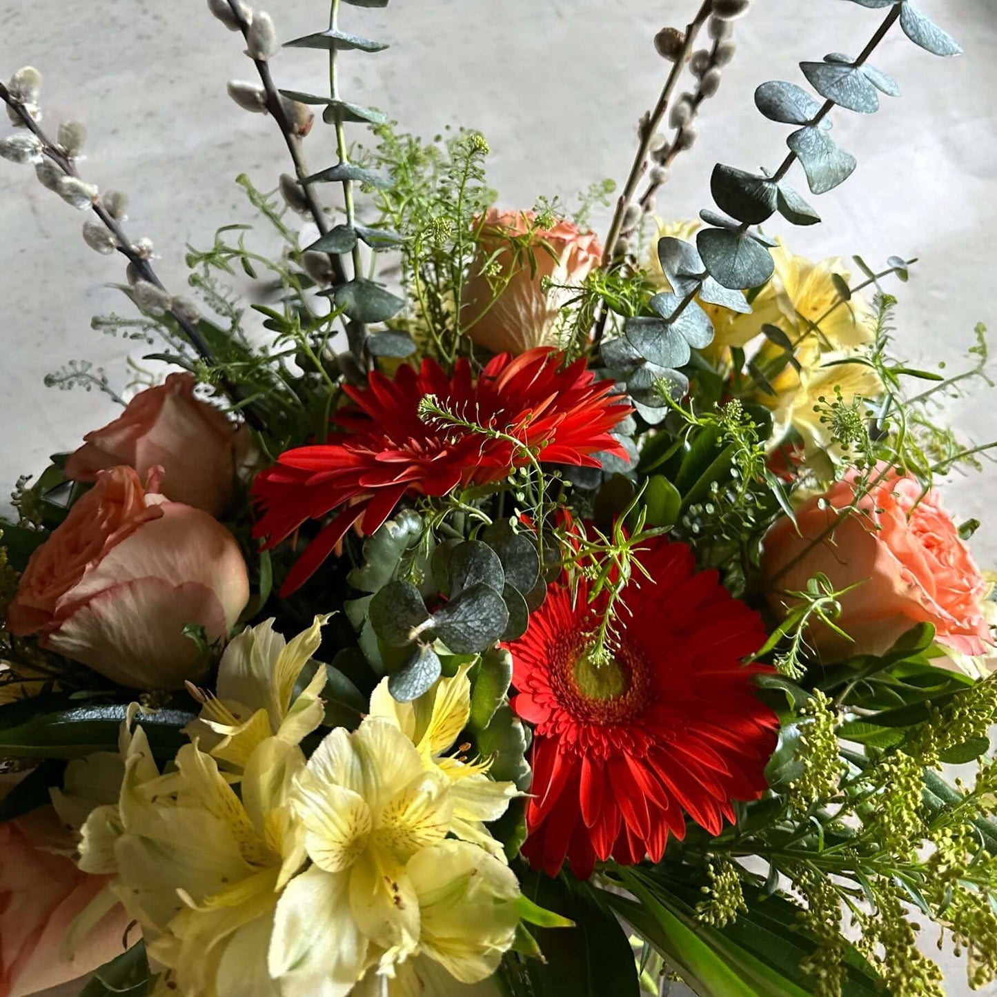 Celestial Serenade floral arrangement with pink roses, red gerberas, and lush greenery in a glass vase.