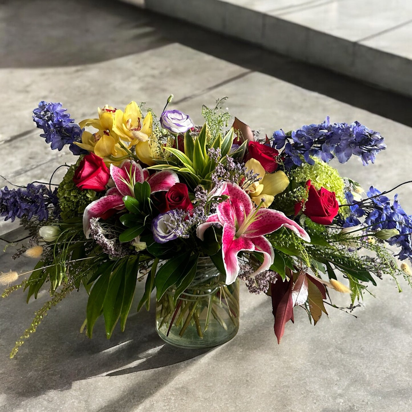 Vibrant Enchanted Garden Bouquet with red roses, pink lilies, yellow orchids, and delphiniums, perfect for Toronto delivery.