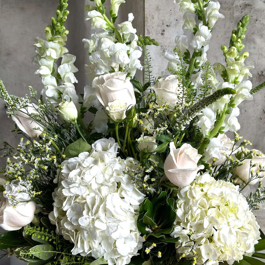 Elegant sympathy flower arrangement with white roses, lilies, and greenery, designed to express love and remembrance