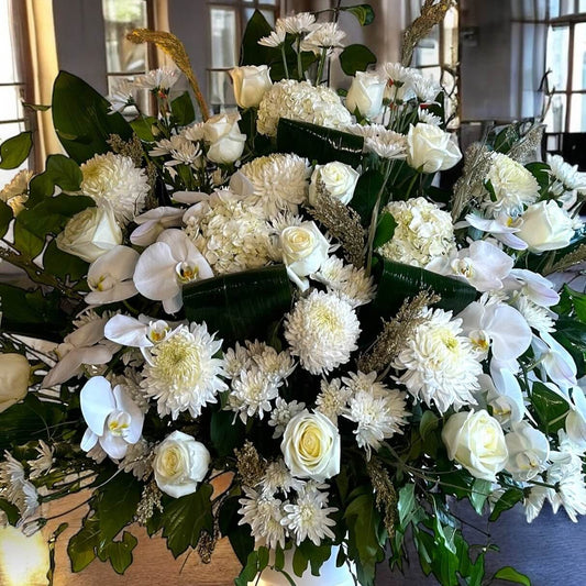 Elegant white sympathy flowers arrangement with roses, orchids, and chrysanthemums for tributes and condolences.