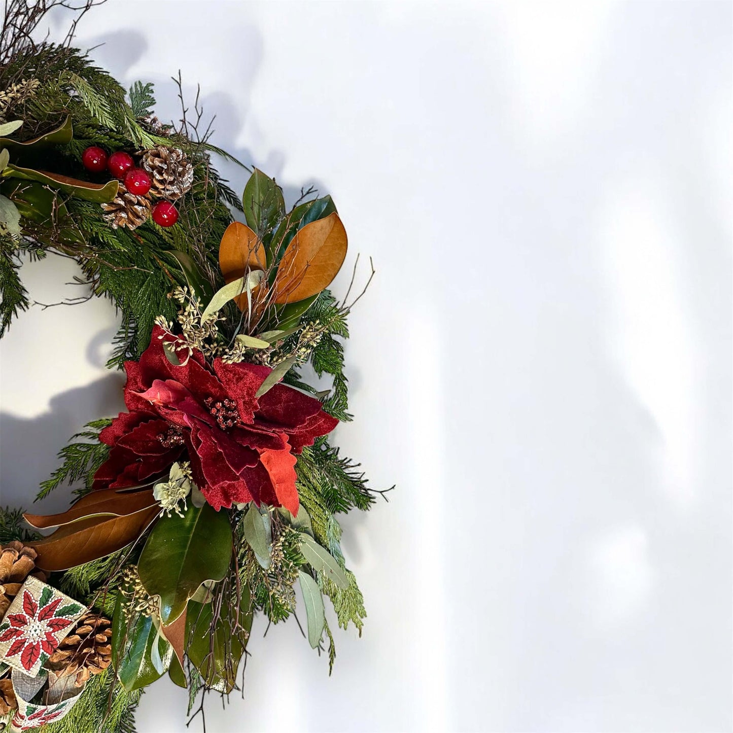 Winter-themed floral wreath with white roses, pinecones, and festive greenery, perfect for holiday decor.