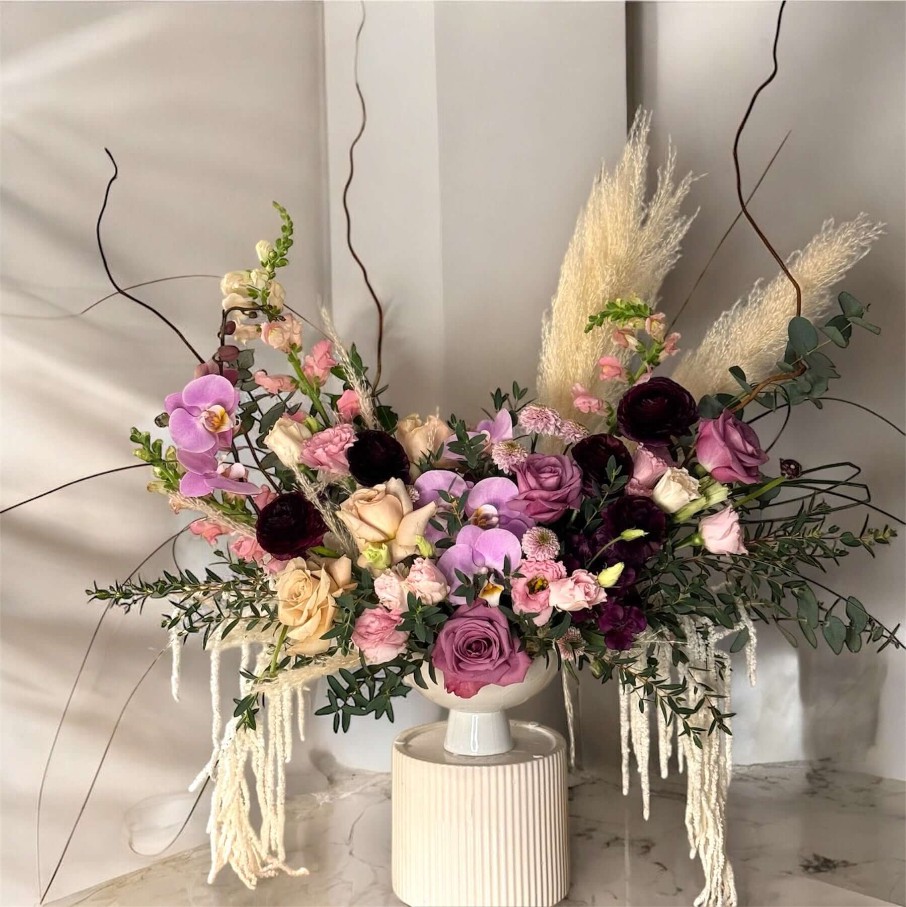 "Chic and modern floral centerpiece with delicate orchids, roses, and pampas grass – perfect for sophisticated home or event decor