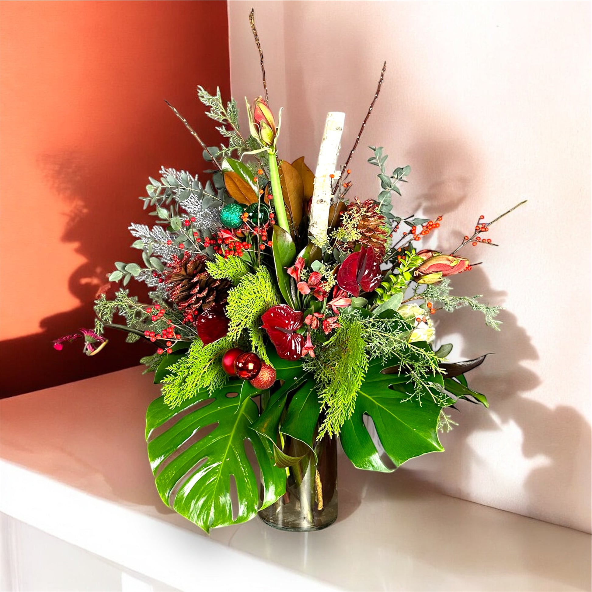 Bouquet of flowers with green leaves and red berries in a clear vase on a white surface.