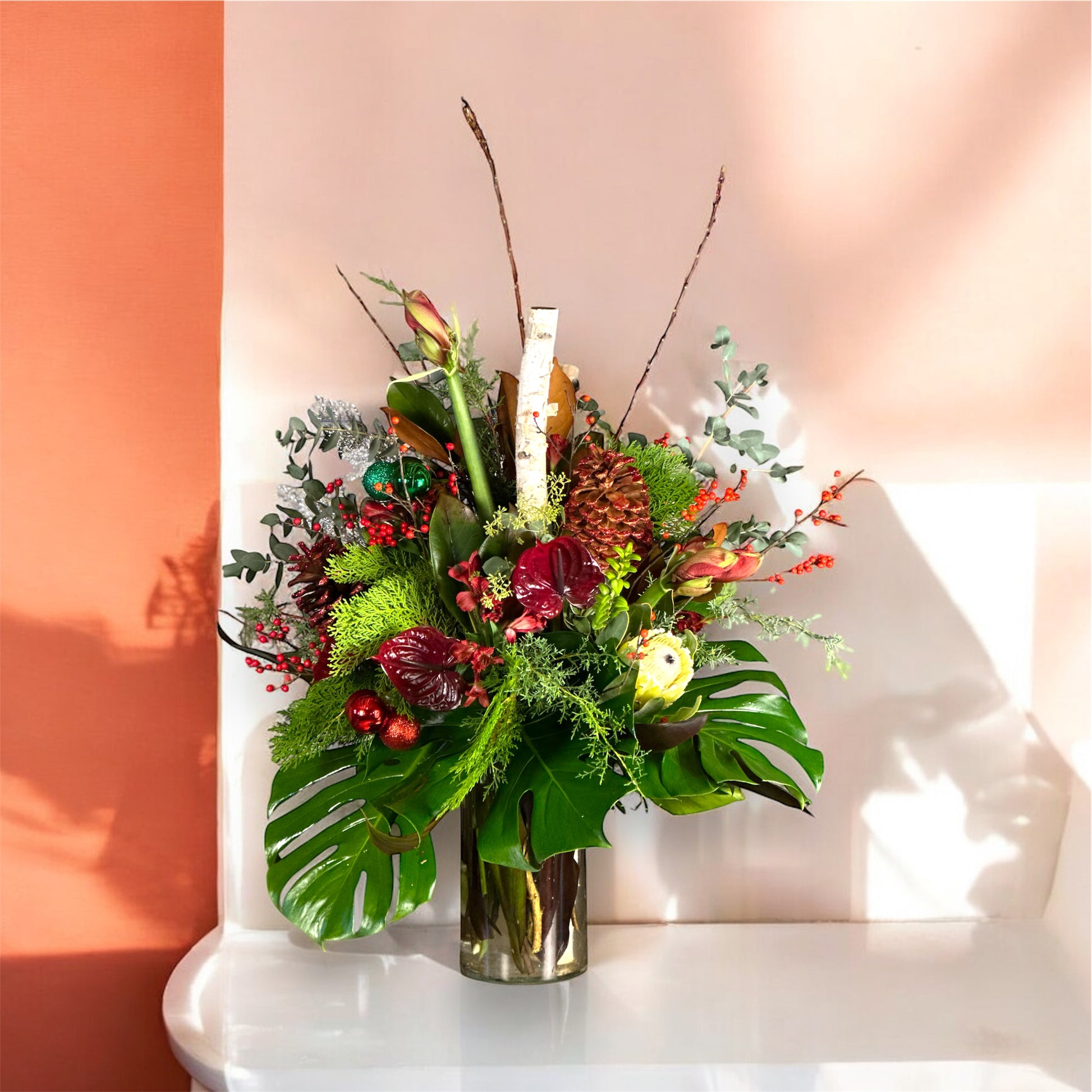 Luxury Christmas floral arrangement with winter greens, red berries, pinecones, and premium blooms in a tall vase.