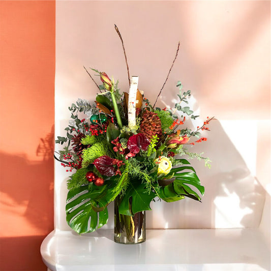 Luxury Christmas floral arrangement with winter greens, red berries, pinecones, and premium blooms in a tall vase.