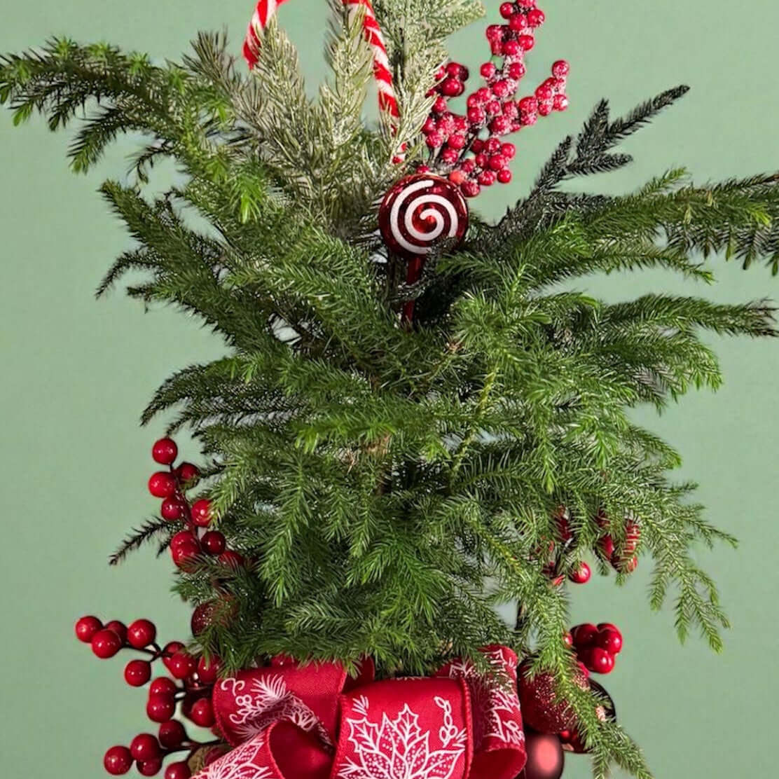 Mini pine tree with red berries, Candy cane ornament, frosted greenery, and red bow in a cream pot.