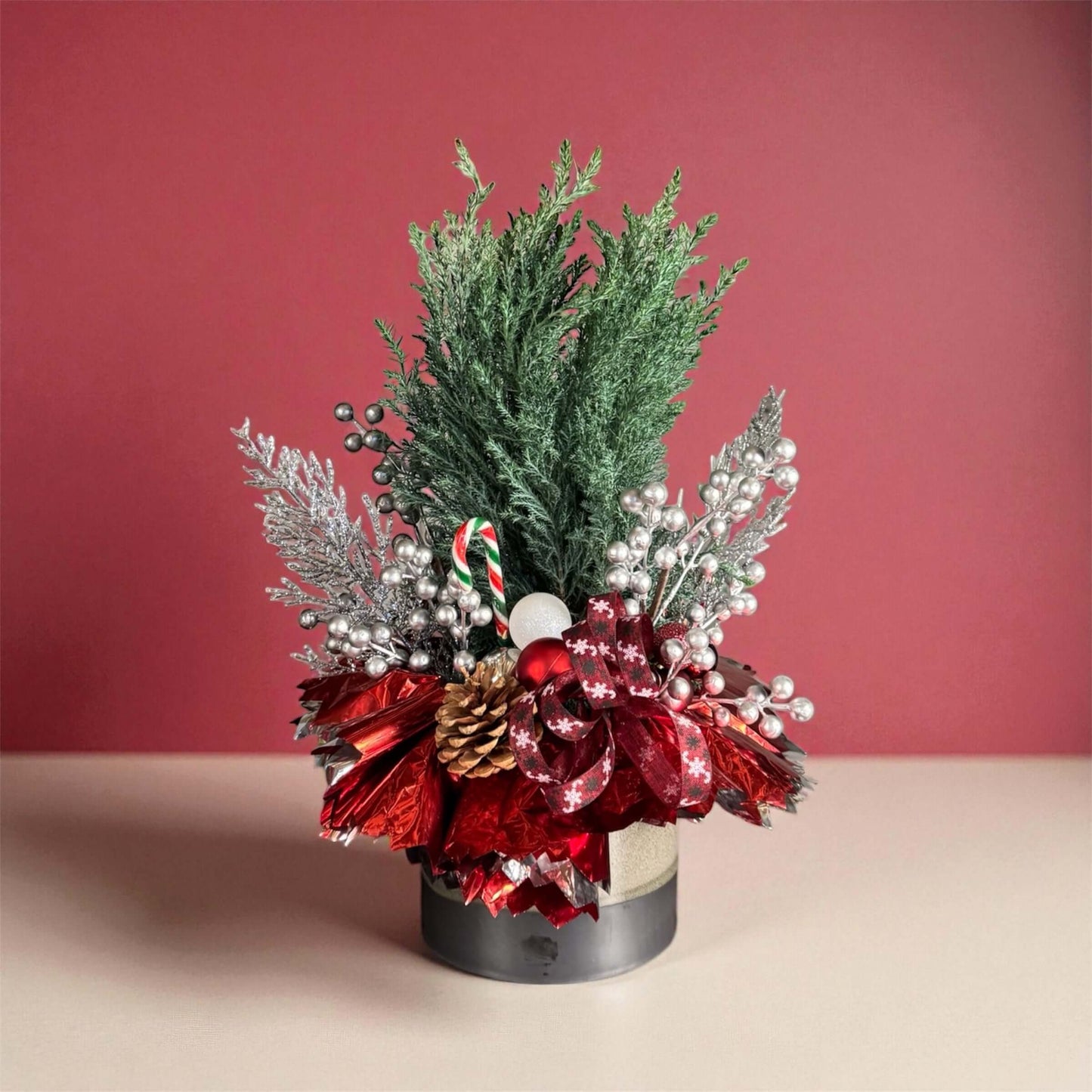 Decorative floral arrangement with red flowers, greenery, and festive elements on a pink background