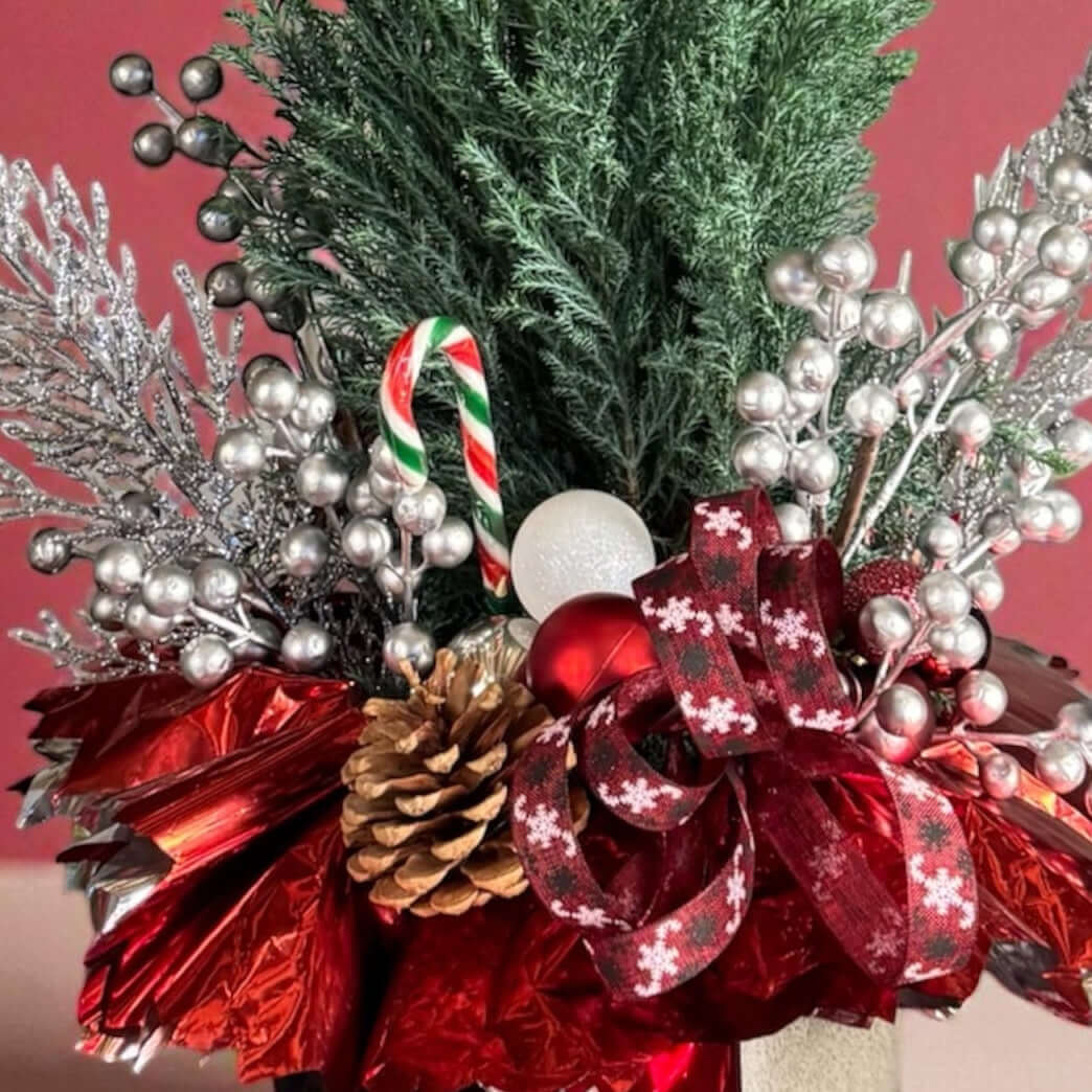 Decorative floral arrangement with red flowers, greenery, and festive elements on a pink background