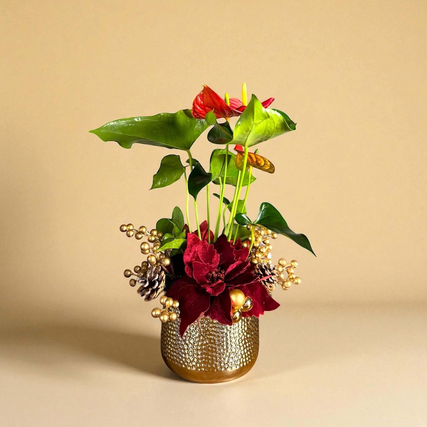 Decorative floral arrangement with red flowers and green leaves in a gold pot on a beige background