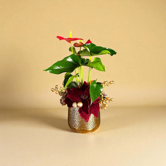 Decorative floral arrangement with red flowers and green leaves in a gold pot on a beige background